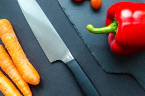 Top view of fresh carrots, red pepper, and tomatoes with a knife on a slate board.